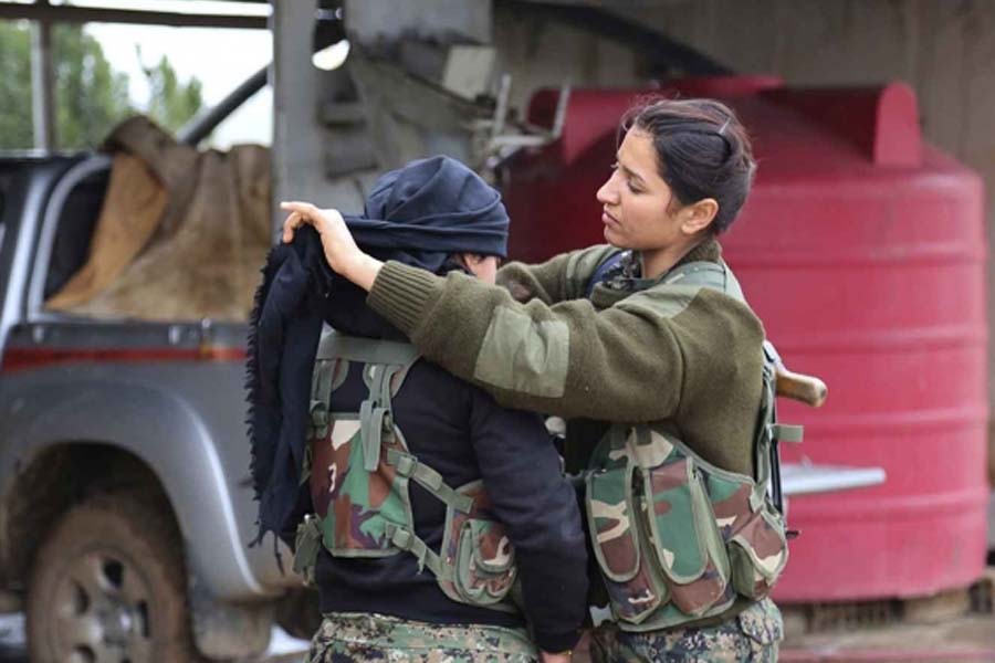 Seorang pejuang wanita Kurdi dari Unit Perlindungan Rakyat (YPG) memasangkan penutup kepala untuk rekannya saat mempersiapkan diri sebelum berangkat ke medan perang dari markasnya, di Qamishli, Suriah, Jumat (19/12).